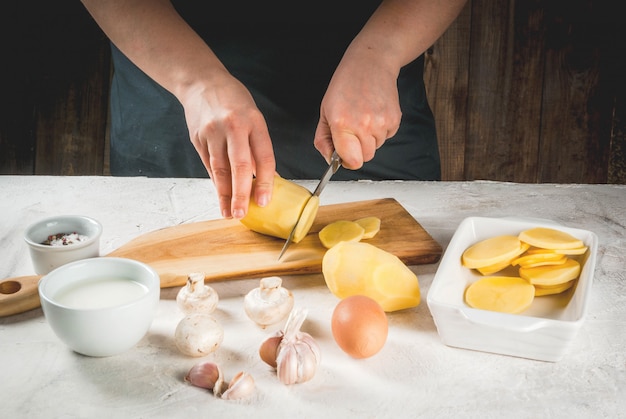 Hands cutting potato surrounded by ingredients