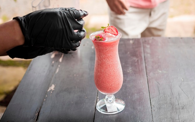 Hands decorating a strawberry smoothie on wooden table Close up of hands making strawberry smoothie on wooden table Close up of person decorating strawberry milkshake on table