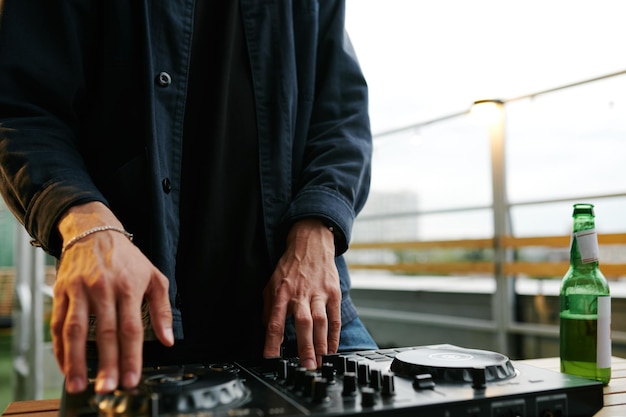 Hands of deejay in black shirt mixing sounds while standing by turntables