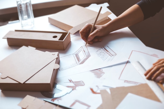 Hands designer draws a sketch of paper packaging. Creative development of ecological boxes.  