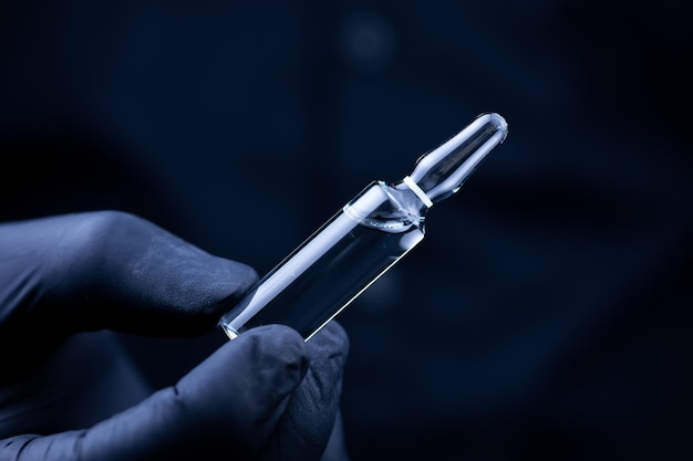 The hands of a doctor in black medical gloves who turns over an ampoule with a vaccine