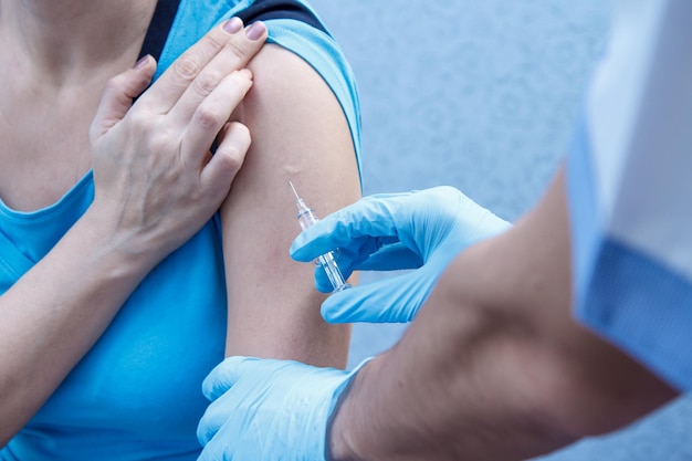 Hands of doctor in blue gloves holding syringe for vaccination to upper arm of patient