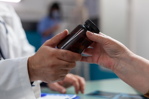 Hands of doctor and senior woman holding bottle of pills in office. Specialist giving flask of medicine to retired adult after medical consultation at checkup appointment. Close up