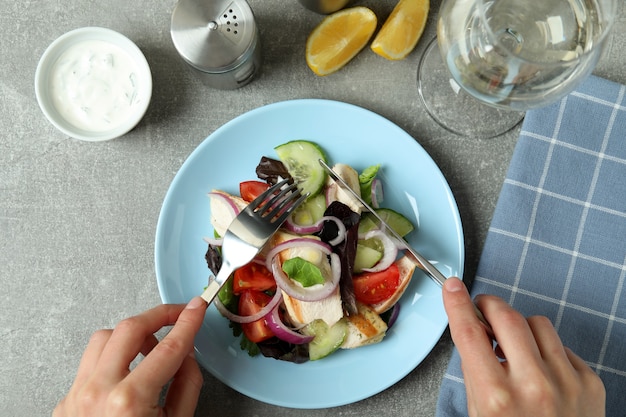 Hands eating salad with grilled chicken on grey table