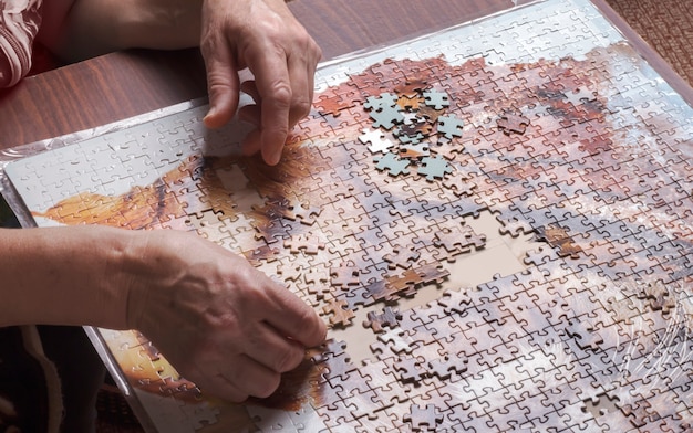 Hands of an elderly woman collecting puzzles on the table.