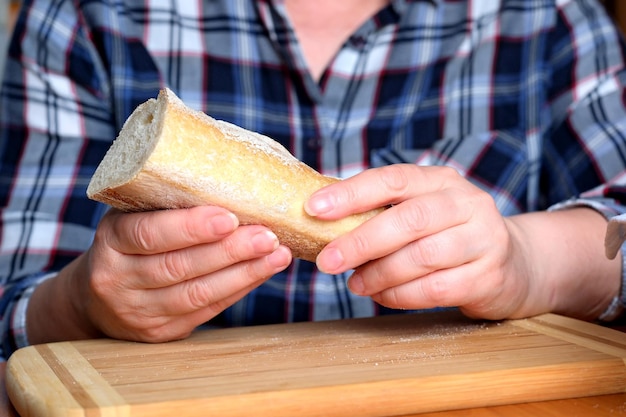 Hands of an elderly woman holding sliced white wheat bread baguette in the kitchen at a brown table no face closeup