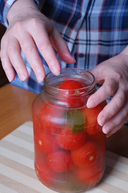 The hands of an elderly woman take out delicious homemade pickled tomatoes from a jar in the kitchen at a brown table without a face closeup