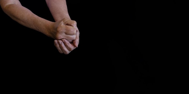 Hands of an elderly woman in wrinkles on a black background closeup