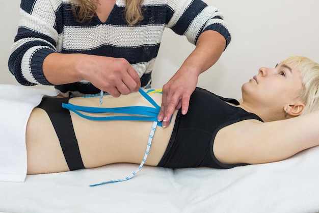 The hands of a female physiotherapist apply adhesive elastic therapeutic tape to the female abdomina