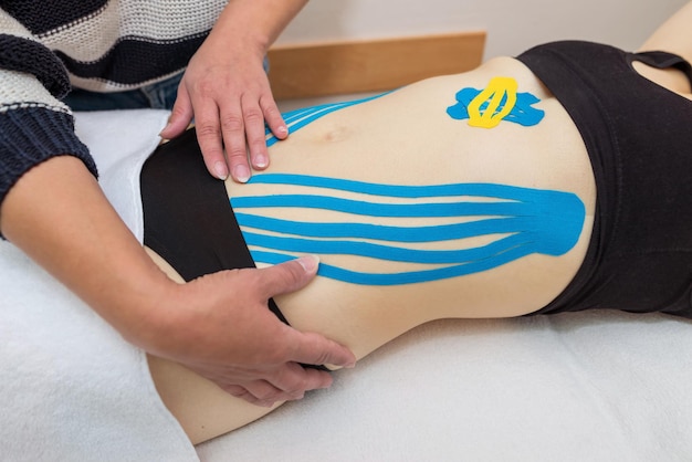 The hands of a female physiotherapist apply adhesive elastic therapeutic tape