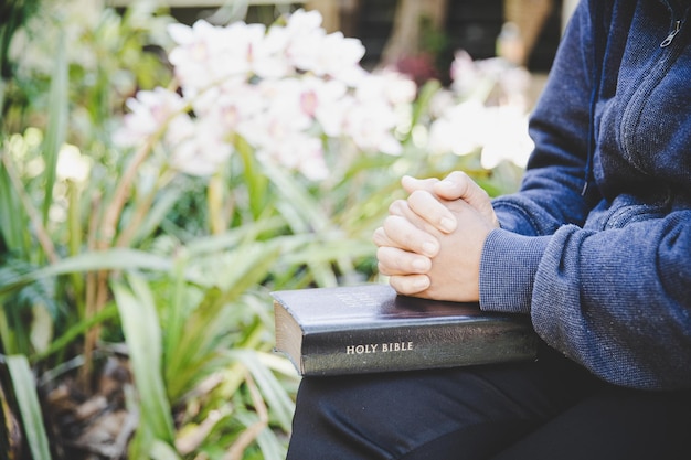 Hands folded in prayer on a Holy Bible in church concept for faith, spirituality and religion