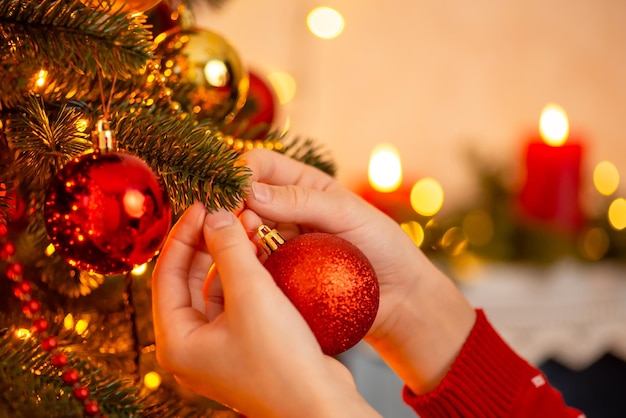 Hands of the girl carefully hanging red ball on the branch of christmas tree