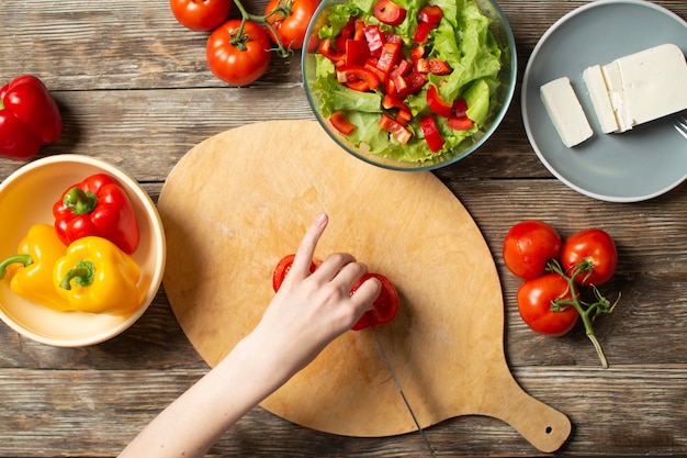 Hands of a girl cut tomates on a wooden table