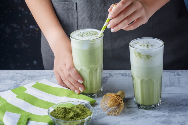 Hands of a girl holding a glass with green latte. Matcha green tea and soy milk drink