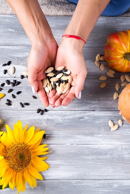 Hands of a girl holding sunflower seeds and a pumpkin on a gray wooden background