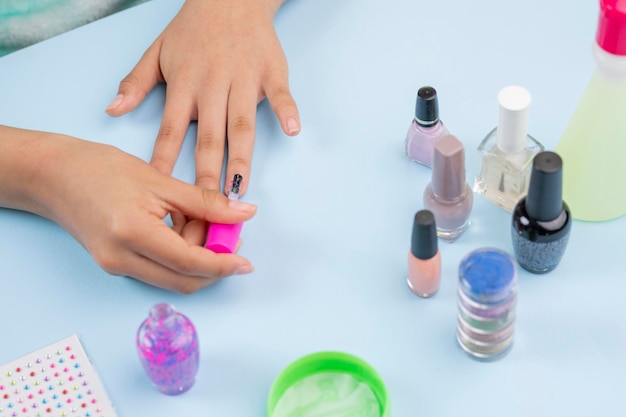 Hands of a girl painting her nails with varnish on a blue table