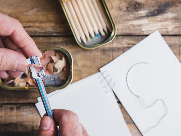 Hands of a girl sharpening a pencil on a wooden table