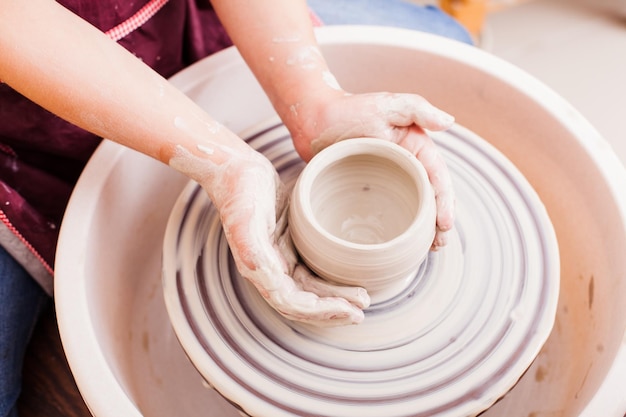 Hands of girl who makes pottery from white clay on a potters wheel