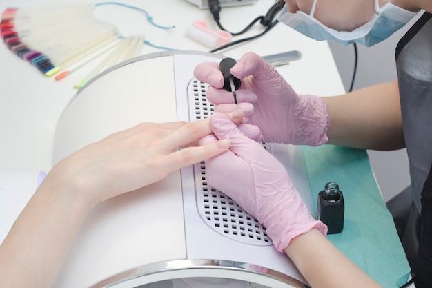 Hands in gloves paint nails in the salon of a manicure. Close up