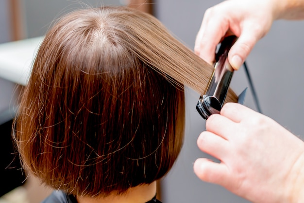 Hands of hairdresser straightening hair of woman.