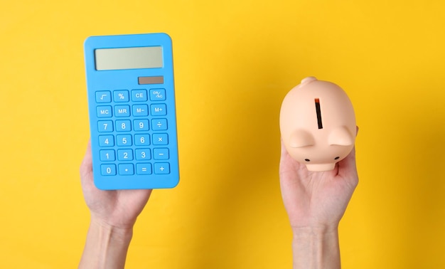 Hands hold calculator and piggy bank on yellow background