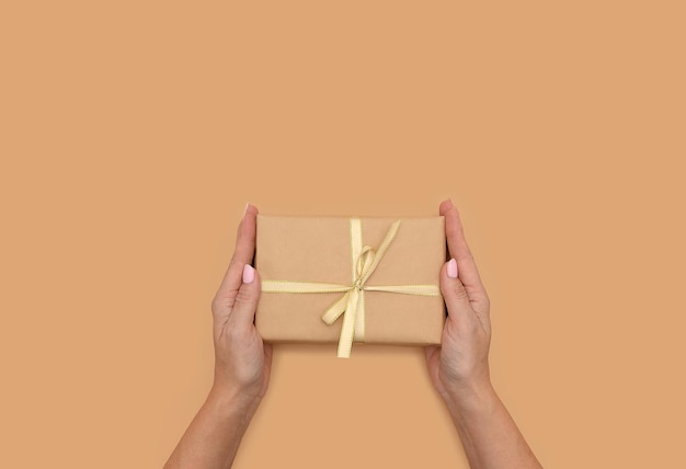 Hands hold a gift box wrapped in kraft paper. On a beige background.