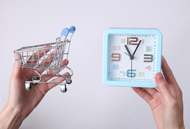 Hands holding alarm clock and shopping trolley on white background Shopping time