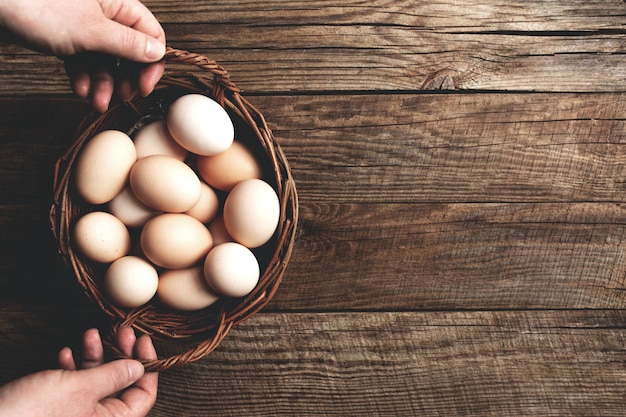 Hands holding basket with chicken eggs on wooden background organic household