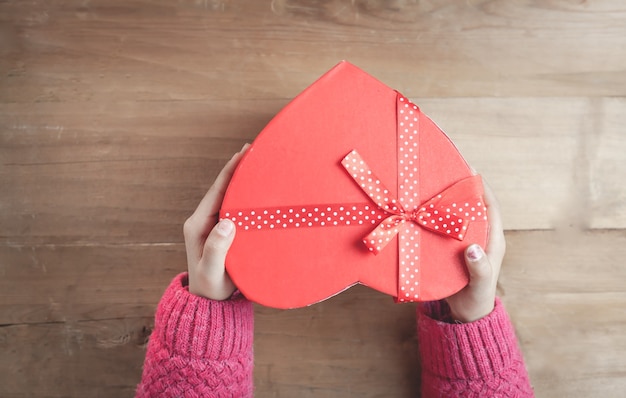 Hands holding a box in the shape of heart on wooden background.