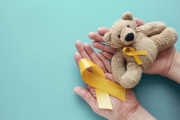 Hands holding children soft toy brown bear with yellow gold ribbon