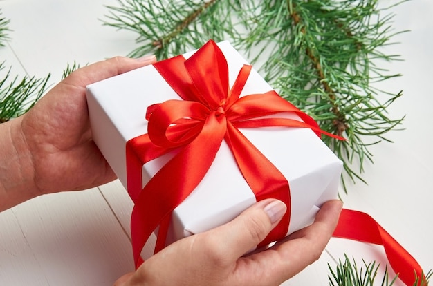 Hands holding Christmas gift box with red ribbon