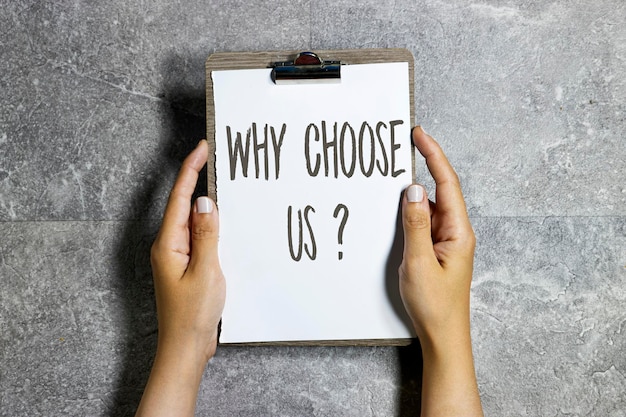 hands holding a clipboard with why choose us question concept on gray grunge marble background