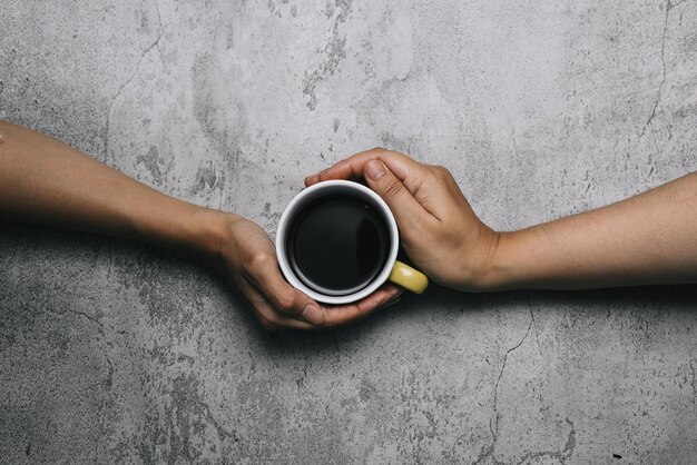 Hands holding coffee drink on cup isolated on gray background, top view.