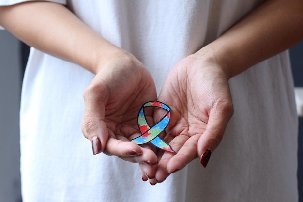 Hands holding colorful autism ribbon shape. Autism spectrum disorder family support concept.