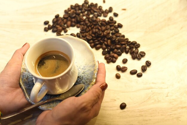 Hands holding a cup of coffee against wooden table and coffee beans