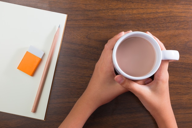 hands holding cup of hot drink and stationary on table