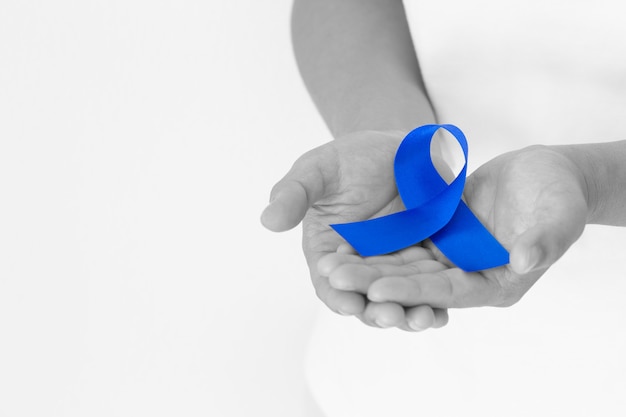 hands holding deep blue ribbon on white fabric with copy space