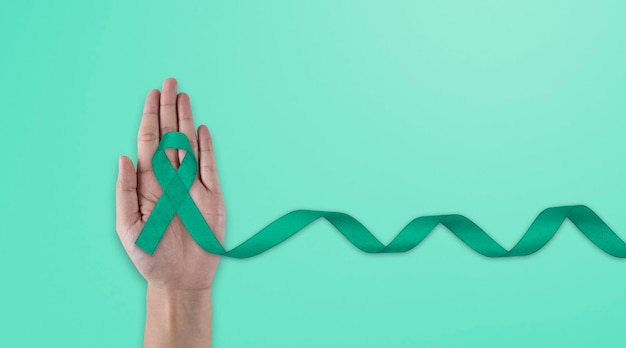 Hands holding emerald green or jade green ribbon on white fabric background with copy space symbol for Liver Cancer awareness World Cancer Day Healthcare