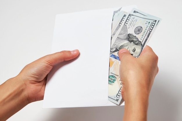 Hands holding envelope with dollar money on white background. Woman hand takes out money from an envelope, close-up. Bribe corruption, salary, earning and savings concept