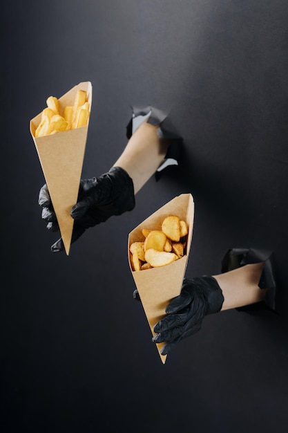 Hands holding french fries through torn holes in black paper background street food concept