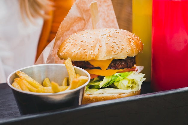 Hands holding fresh delicious burger with french fries on the black wooden table