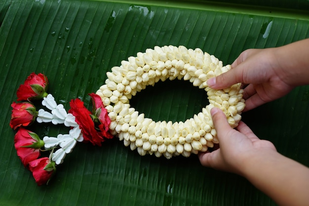 Hands holding a garland made of jasmine and roses on green leaves