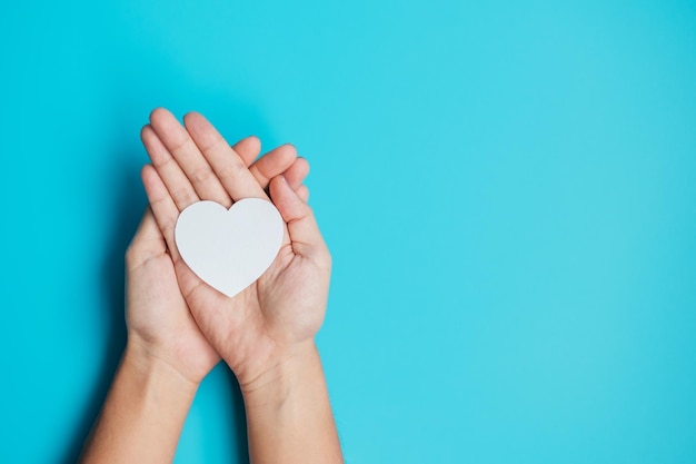 Hands holding paper Heart on blue background Donation Wellness world Heart day world Health day and Happy Valentines day concepts