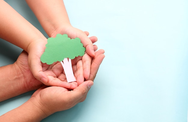 Hands holding paper tree on blue.