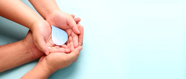 Hands holding paper water drop on blue background.