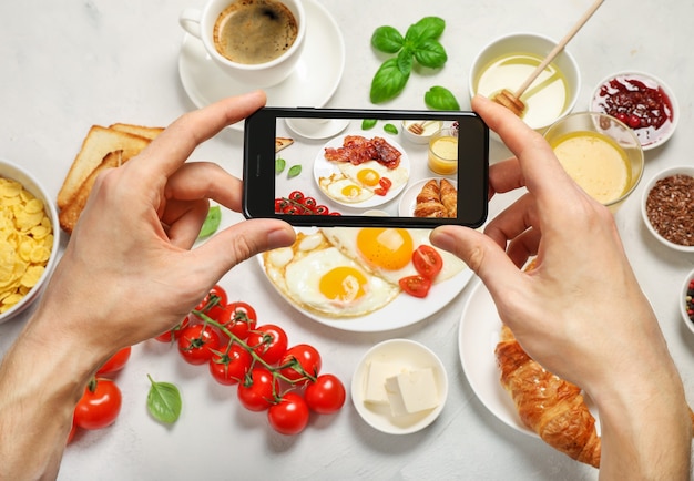 Hands holding phone and taking photo of breakfast flat lay.