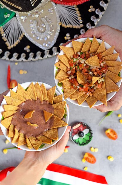 Hands holding plates with Totopos tortilla with bean sauce and pico de gallo