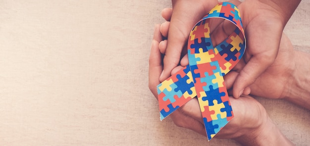 Hands holding puzzle ribbon for autism awareness banner