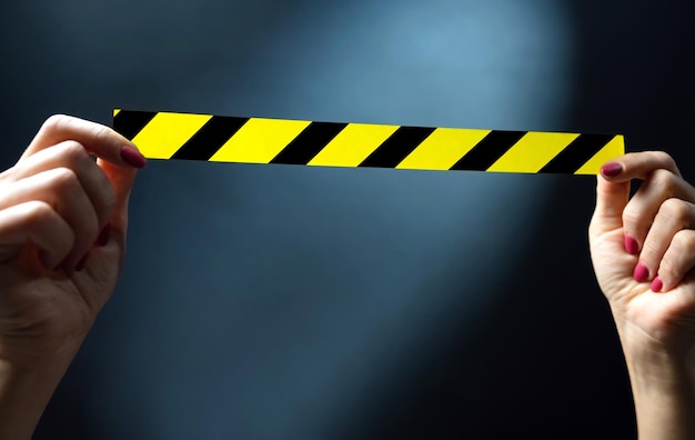 Hands holding yellow tape with black and yellow stripes on a dark background  warning ribbon