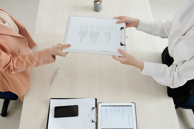 Hands of HR manager asking applicant to give her printed curriculum vitae document, view from above